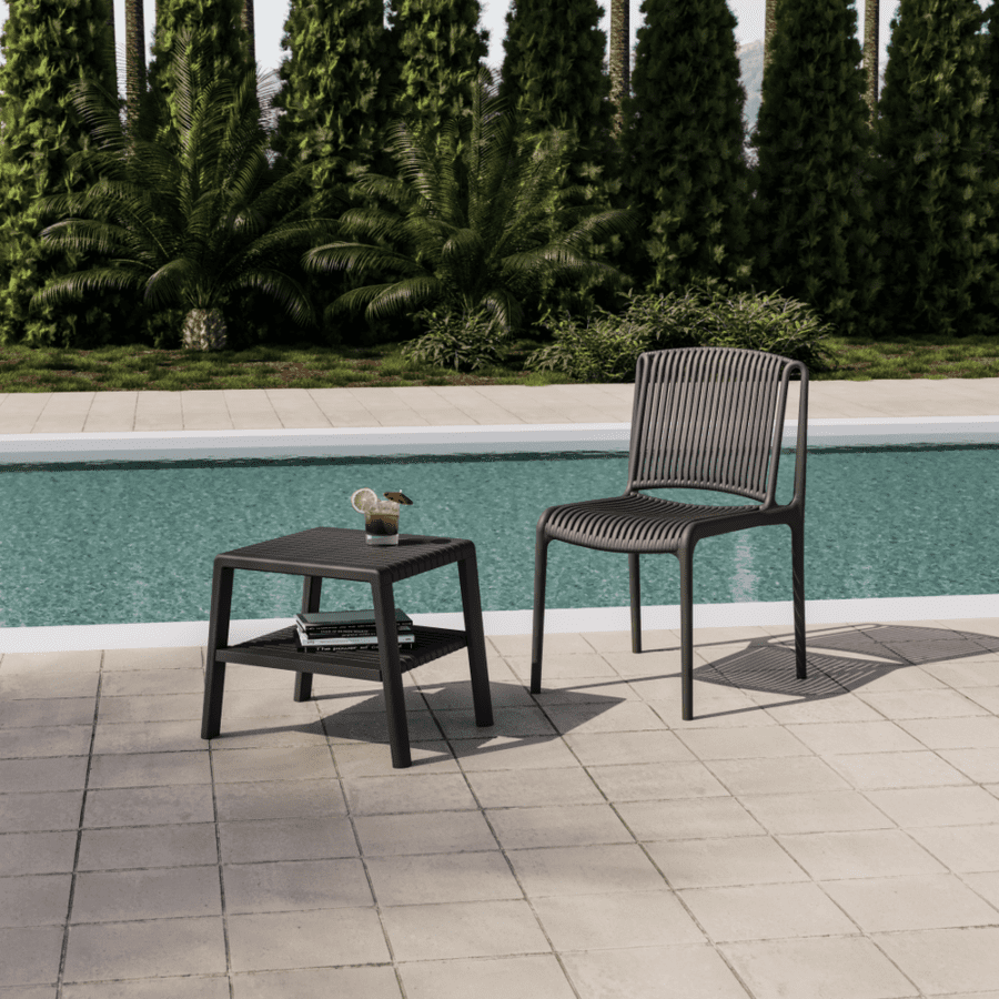 Outdoor plastic chair and matching side table displayed beside a resort-style swimming pool, surrounded by lush landscaping and commercial outdoor planters in a contemporary hospitality setting.