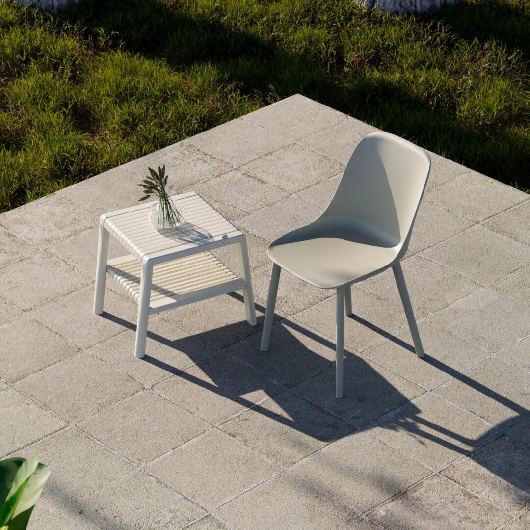 Ivory white Joker outdoor commercial coffee table with slatted lower shelf beside a modern outdoor chair on a stone patio with natural green grass backdrop.